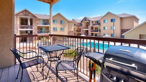 A balcony with outdoor seating, a grill, and a view of a swimming pool and apartment buildings. - 6B Cozy Moab Redcliff Condo, Pet Friendly, Pool & Hot Tub (Moab)