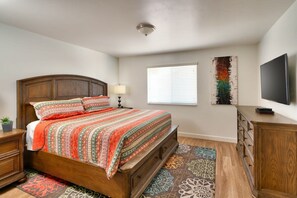 A bedroom with a wooden bed, a nightstand, a dresser, a TV, and a window with blinds. - 6B Cozy Moab Redcliff Condo, Pet Friendly, Pool & Hot Tub (Moab)
