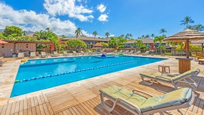 A pool area with lounge chairs and umbrellas, surrounded by palm trees and buildings.