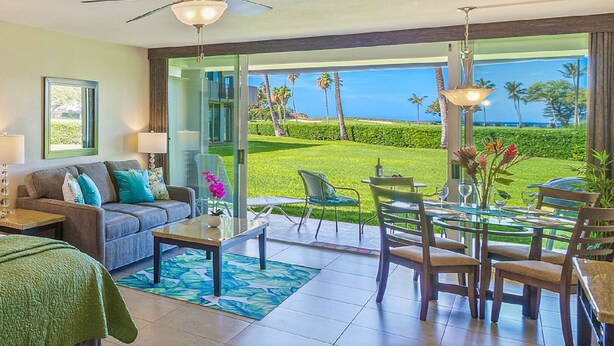 A hotel room with a balcony, a sofa, a dining table, and chairs.