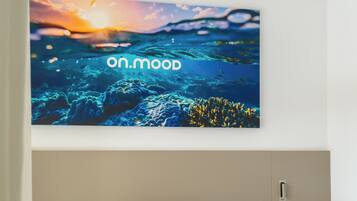 A hotel room with a bed, a nightstand, and a wall-mounted TV displaying a scenic underwater image with the text "on.mood".