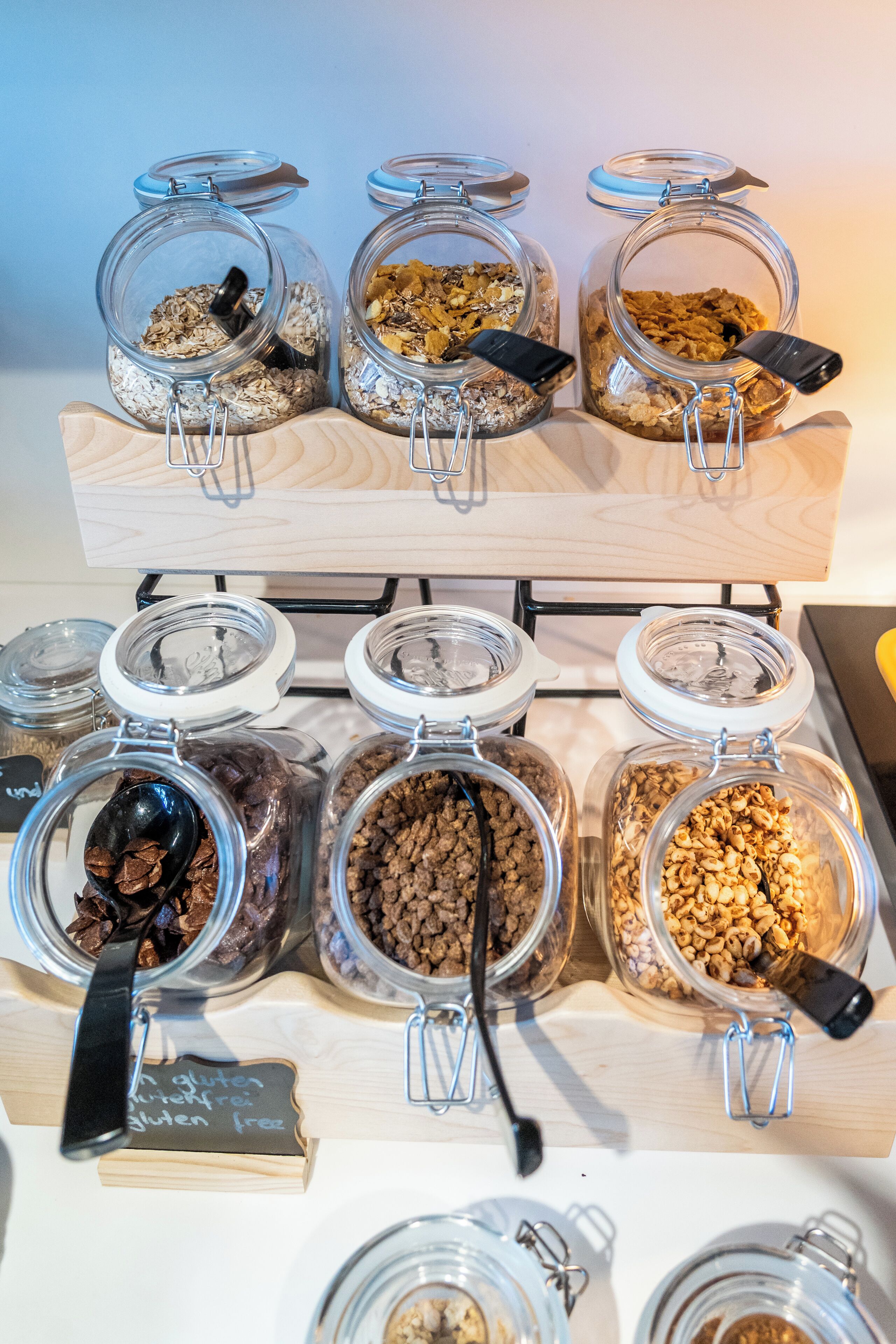 A display of various food items in glass jars with metal clasps, arranged on a wooden shelf.