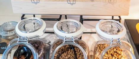 A display of various food items in glass jars with metal clasps, arranged on a wooden shelf.
