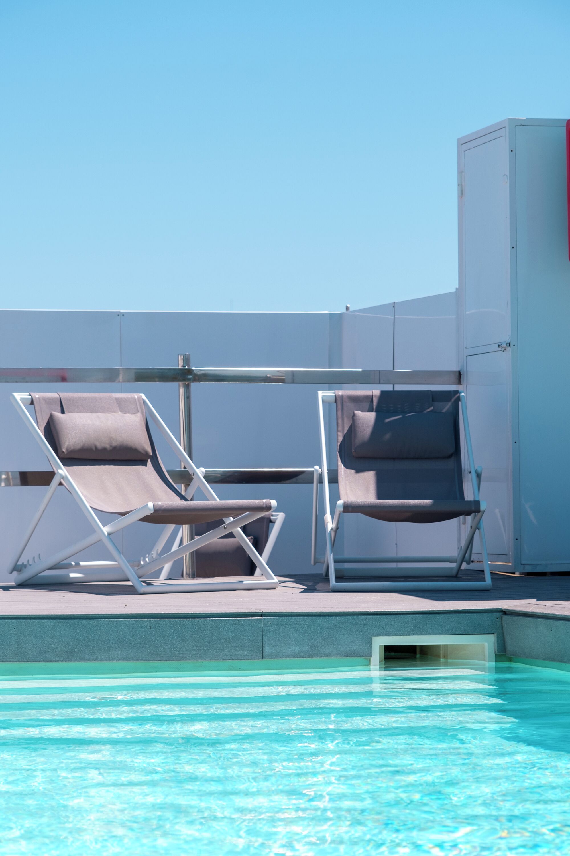 Un área junto a la piscina con dos sillas reclinables y barandilla de vidrio.