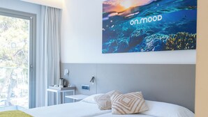 Una habitación de hotel moderna con una cama grande, una manta verde, una mesita de noche, una lámpara y una obra de arte en la pared que representa una escena submarina.