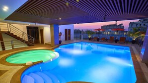 En indendørs swimmingpool med træterrasse, trappe og udsigt til solnedgangen.