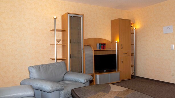 A living room with a grey sofa, a television, and a wooden cabinet.
