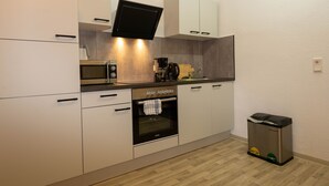 A modern kitchen with white cabinets, a built-in microwave, a coffee maker, and a trash bin.