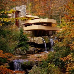 Uma casa moderna com fachada de pedra, telhado plano e uma cascata na frente.