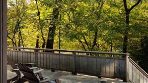 A wooden deck with Adirondack chairs and a table, overlooking a forested area. - Riverside Chalet Plus (Confluence)