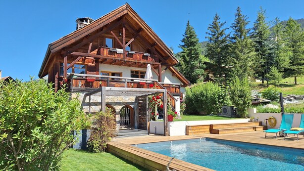 Una cabaña con terraza de madera, piscina y un arco de piedra.