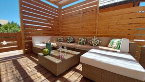Una terraza de madera con un sofá de mimbre, una mesa de centro de vidrio y una sandía.
