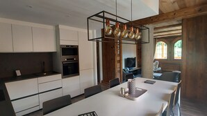 Una cocina moderna con armarios blancos, horno empotrado y comedor con mesa y sillas blancas.