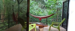 A balcony with a hammock, wooden table, and two chairs, surrounded by lush greenery. - Selva Linda Lodge (Quepos)