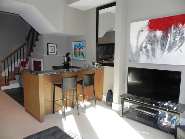 Una cocina moderna con barra, televisor grande y escalera.