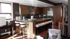 A modern kitchen with a central island, bar stools, stainless steel appliances, and wooden cabinetry. - FAB FITZWALK Townhome FAMILY GETAWAY! Hot Tub, 2 car garage, minutes to Village (Whistler)
