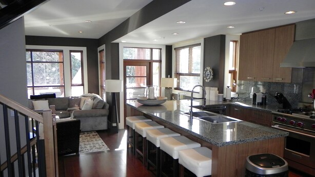 A modern kitchen with a central island, bar stools, a sink, and a stove. - FAB FITZWALK Townhome FAMILY GETAWAY! Hot Tub, 2 car garage, minutes to Village (Whistler)