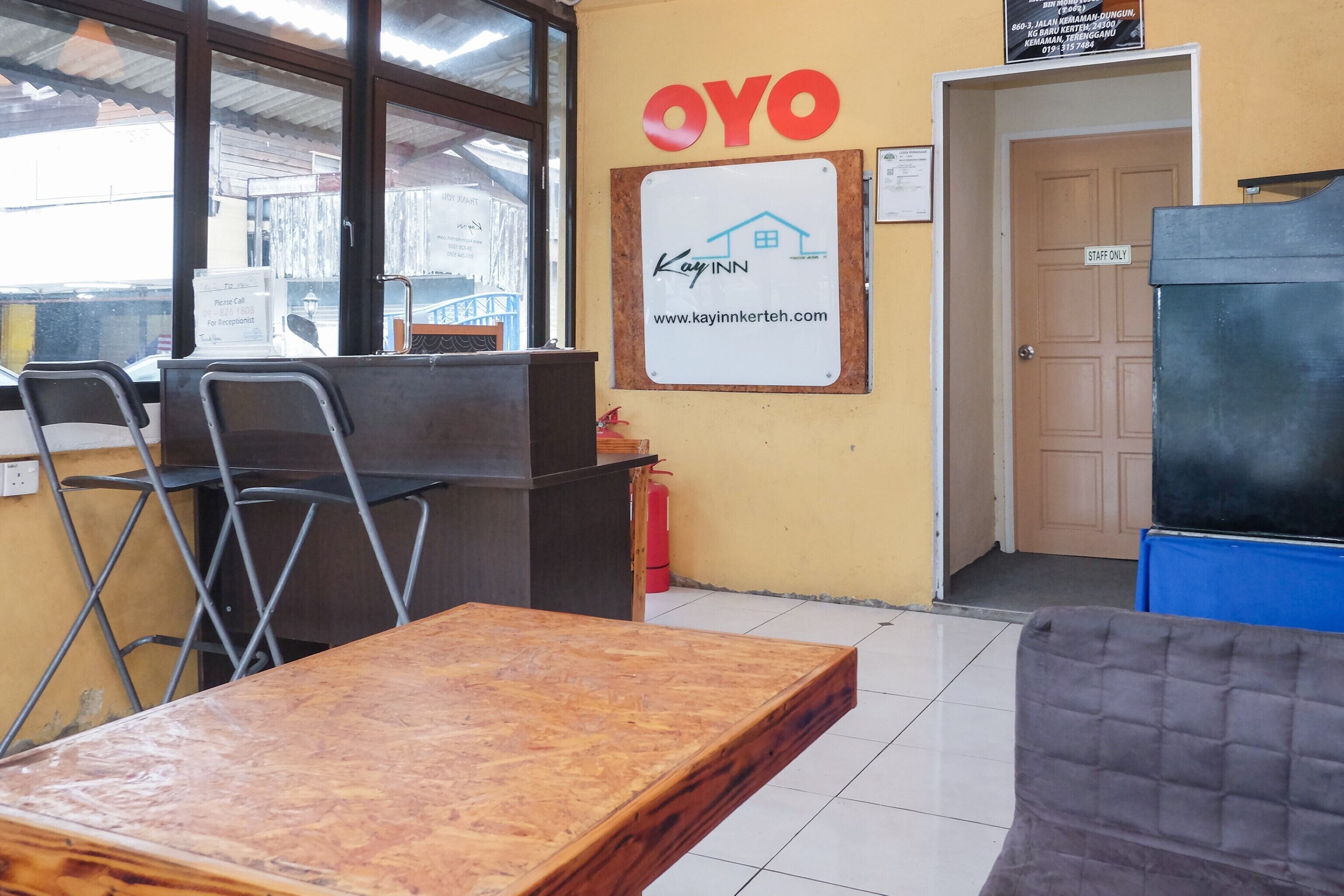 Un área de recepción con un escritorio de madera, sillas de metal, un letrero de 'OYO' y un letrero de 'Kayinn Kerteh'.
