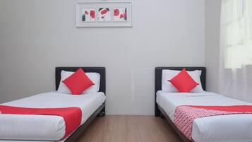 A hotel room with two single beds, each with white bedding and red pillows, a framed artwork above the beds, and a wooden floor.