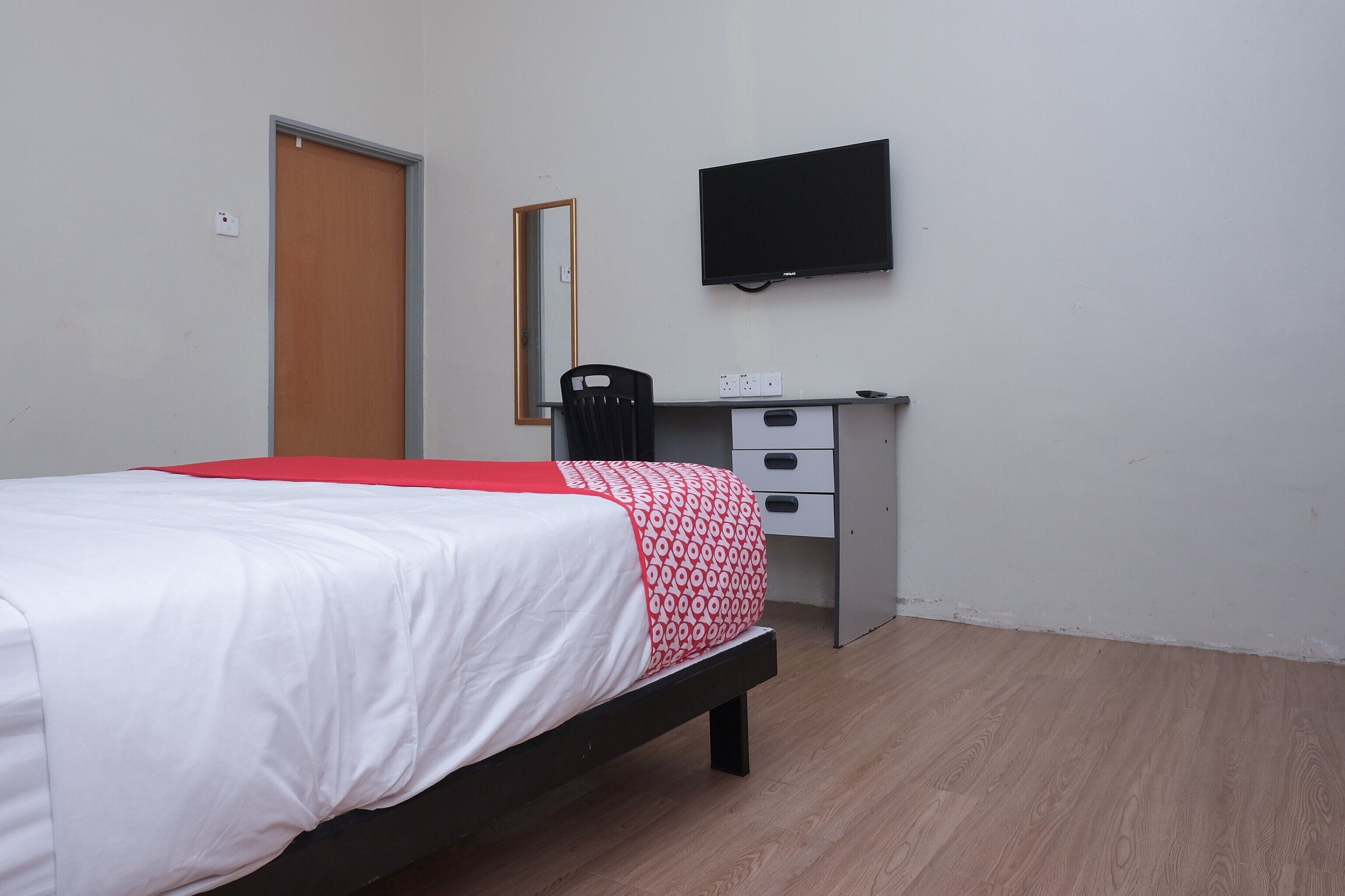 A bedroom with a bed, a desk, a chair, a television, and a mirror.