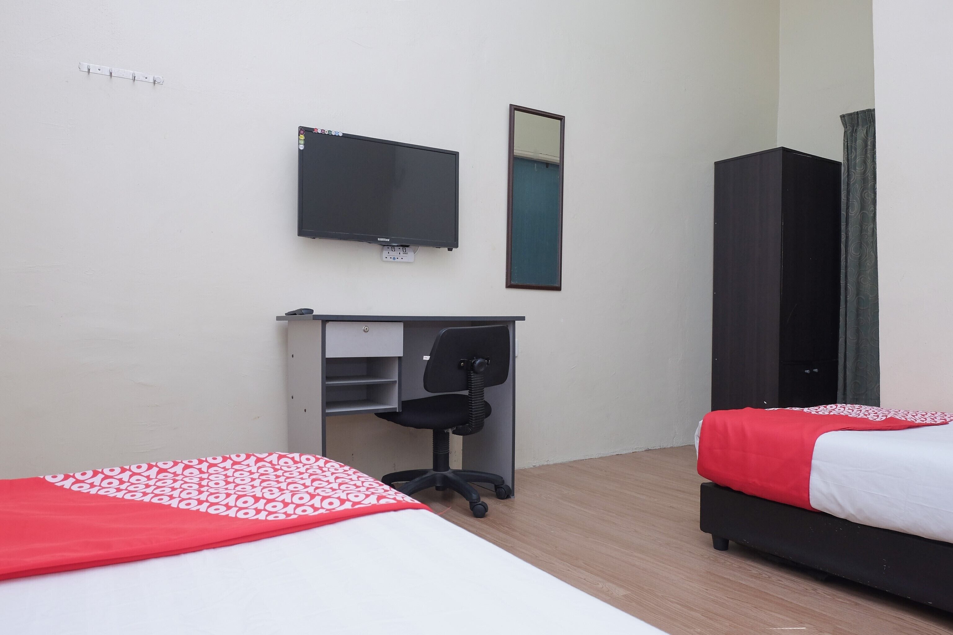 A hotel room with two beds, a desk with a chair, a flat-screen TV, and a wardrobe.