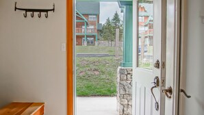 A doorway leading to a porch with a bench, a stone wall, and a view of a building with a green roof. - Camp 4 24: Slope Side, Cozy 2 BR with Shuttle Service (Snowshoe)
