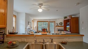 A kitchen with a double sink, wooden cabinets, a ceiling fan, and a window with blinds. - Camp 4 24: Slope Side, Cozy 2 BR with Shuttle Service (Snowshoe)