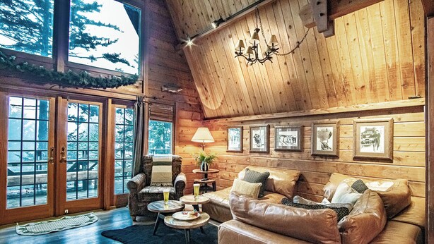 A log cabin interior with a leather sofa, a wooden coffee table, and a chandelier.