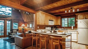 A cozy cabin-style kitchen with wooden cabinets, a central island with stools, and a refrigerator.