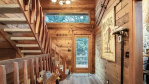 A wooden interior with a staircase, a door leading outside, and a poster on the wall.
