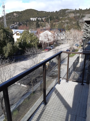 En balkong med ett metallräcke som vetter ut mot en gata där bilar är parkerade, och med byggnader i bakgrunden.