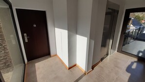 A modern hallway with a dark door labeled '11', a glass door leading outside, and a tiled floor. - La Esquina (San Martín de los Andes)