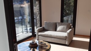 A modern living room with a sofa, a glass coffee table, and large windows offering a view of the outside. - La Esquina (San Martín de los Andes)