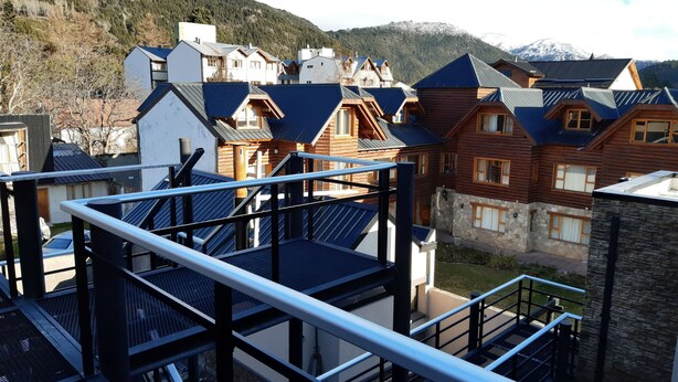 A residential area with a mix of modern and traditional wooden houses, a metal staircase, and a view of snow-capped mountains. - La Esquina (San Martín de los Andes)