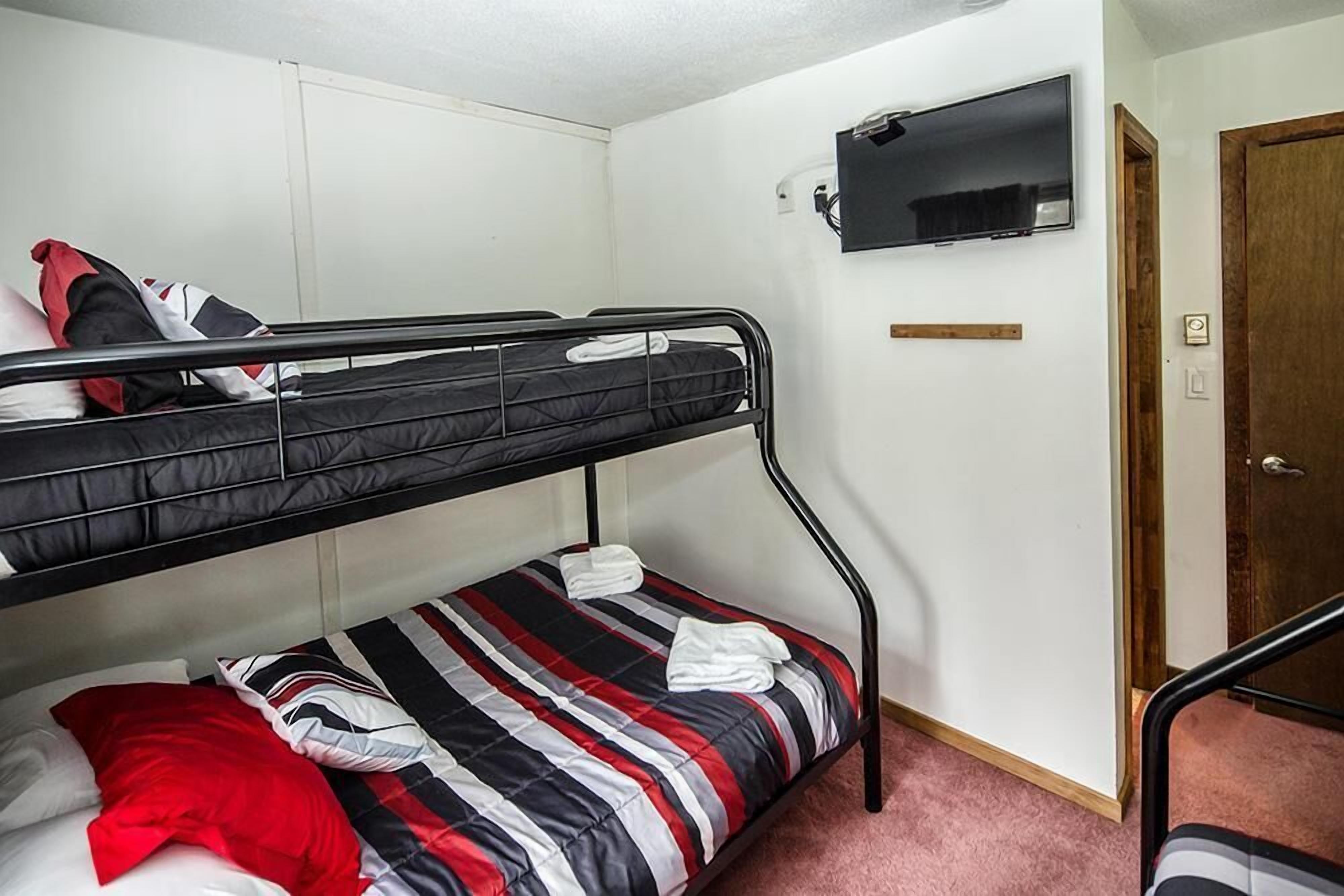 A bunk bed room with a TV mounted on the wall and a door to the right.