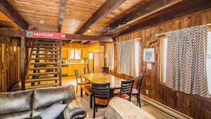 Interior acogedor de una cabaña con comedor, sofás de cuero y una escalera con la etiqueta 'FROSTLINE'.