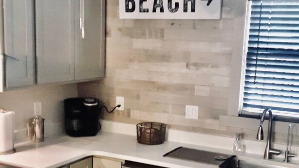 Een kleine keuken met een plafondventilator, een wasmachine en een spoelbak. Een bord op de muur geeft aan: 
