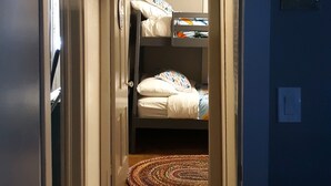 Een smalle gang die leidt naar een slaapkamer met een stapelbed, een kamerbreed tapijt met patroon en een deur naar een andere kamer.