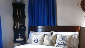 Een slaapkamer met een bed, een plafondventilator, een nachtkastje en een dressoir.