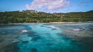Paisaje costero con aguas turquesas cristalinas, una playa de arena y una colina con un edificio.