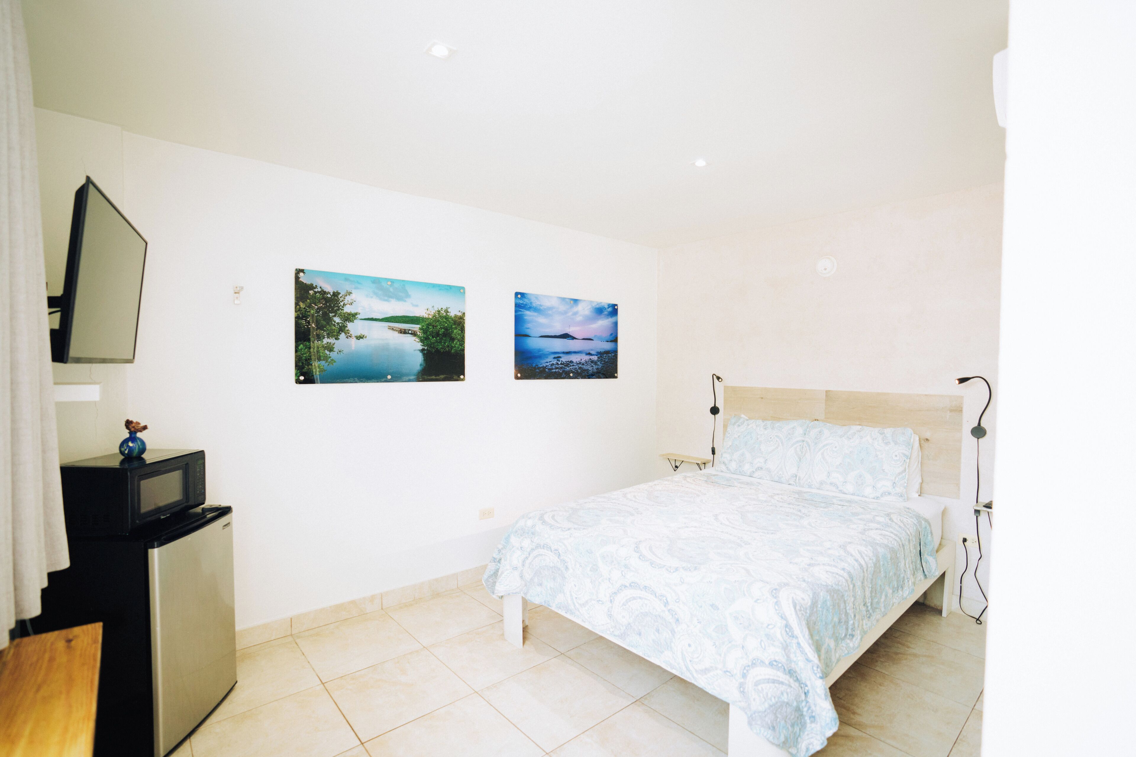 A bedroom with a bed, a small desk with a microwave, and two landscape pictures on the wall.