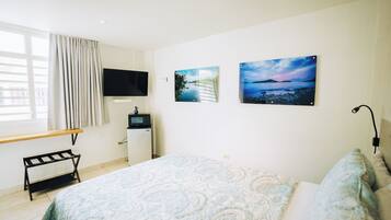 Een slaapkamer met een bed, een televisie, een bureau en twee foto's aan de muur.