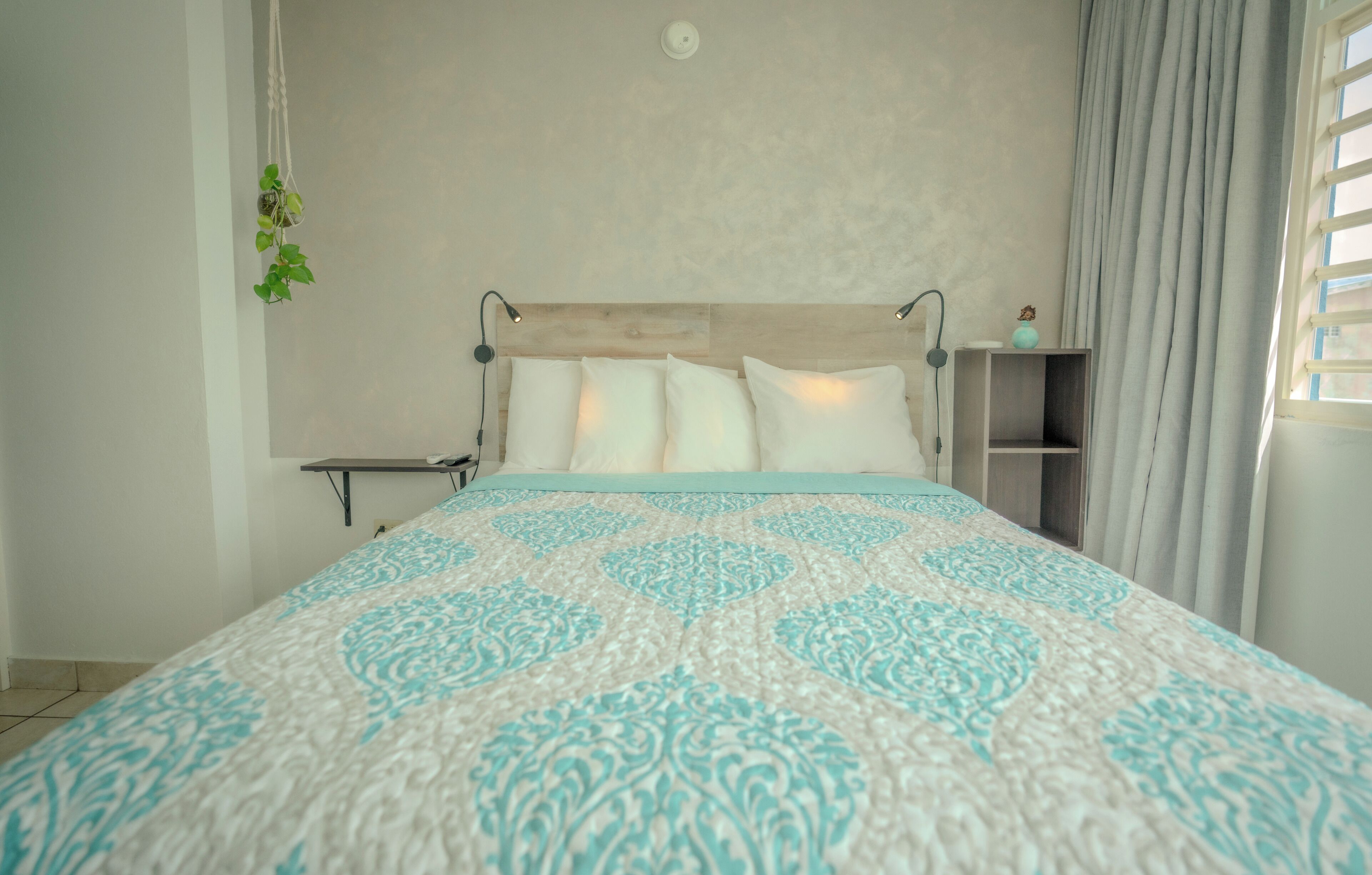 A neatly made bed with a patterned bedspread, a bedside table with a lamp, and a small shelf with a decorative item.