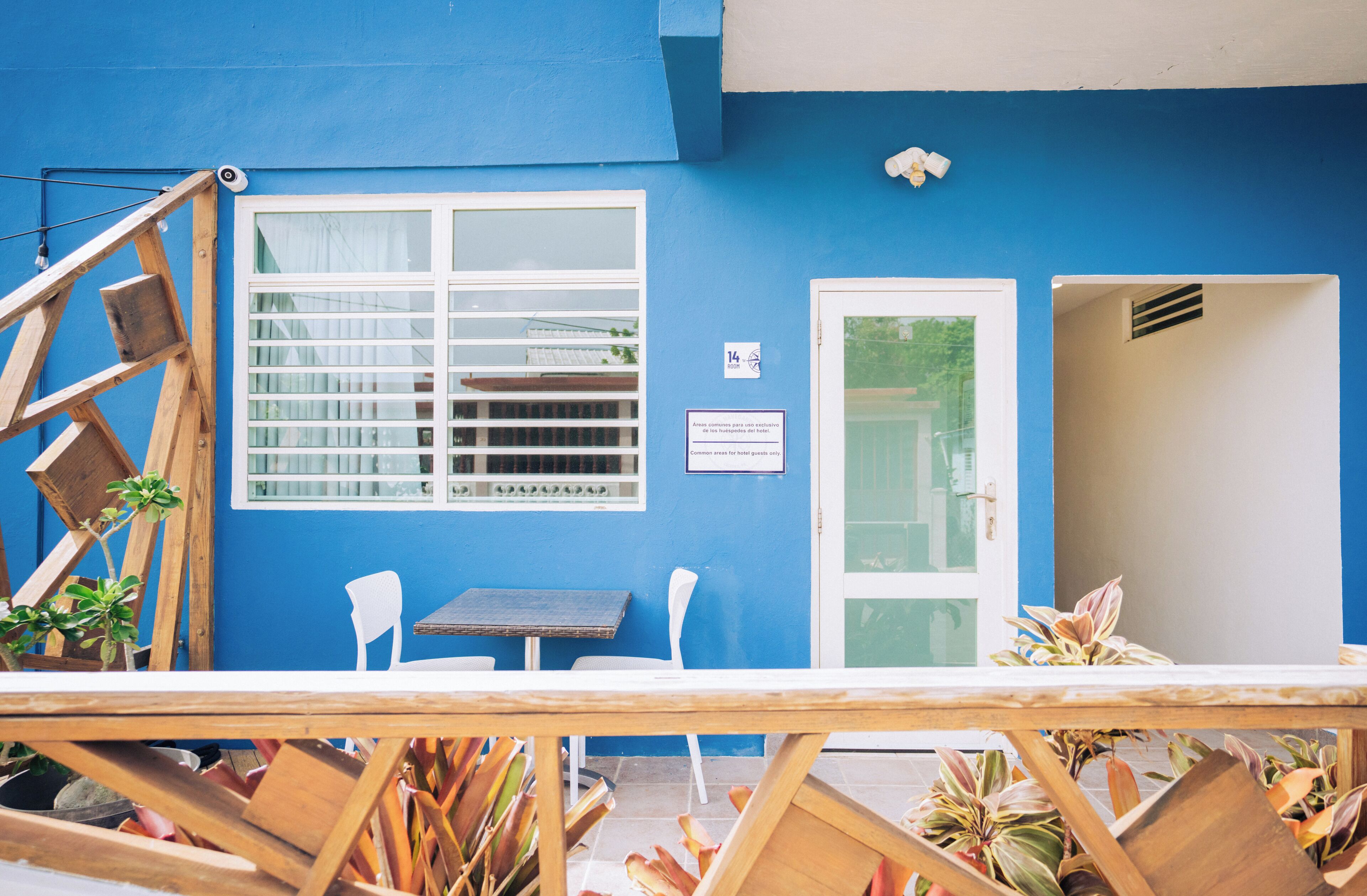 A blue building with a white door, a window with bars, and a small table with two chairs.