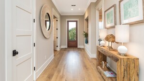 A hallway with a wooden floor, white doors, a wooden console table with decorative items, and framed artwork on the walls. - CLOSE TO CHARLESTON/ROOFTOP/LUXURY AMENTIES/POOL/OCEAN VIEW/FANTASTIC FALL RATES (Isle of Palms)