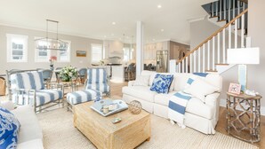 A spacious living room with a high ceiling fan, a staircase, and a kitchen in the background. - CLOSE TO CHARLESTON/ROOFTOP/LUXURY AMENTIES/POOL/OCEAN VIEW/FANTASTIC FALL RATES (Isle of Palms)