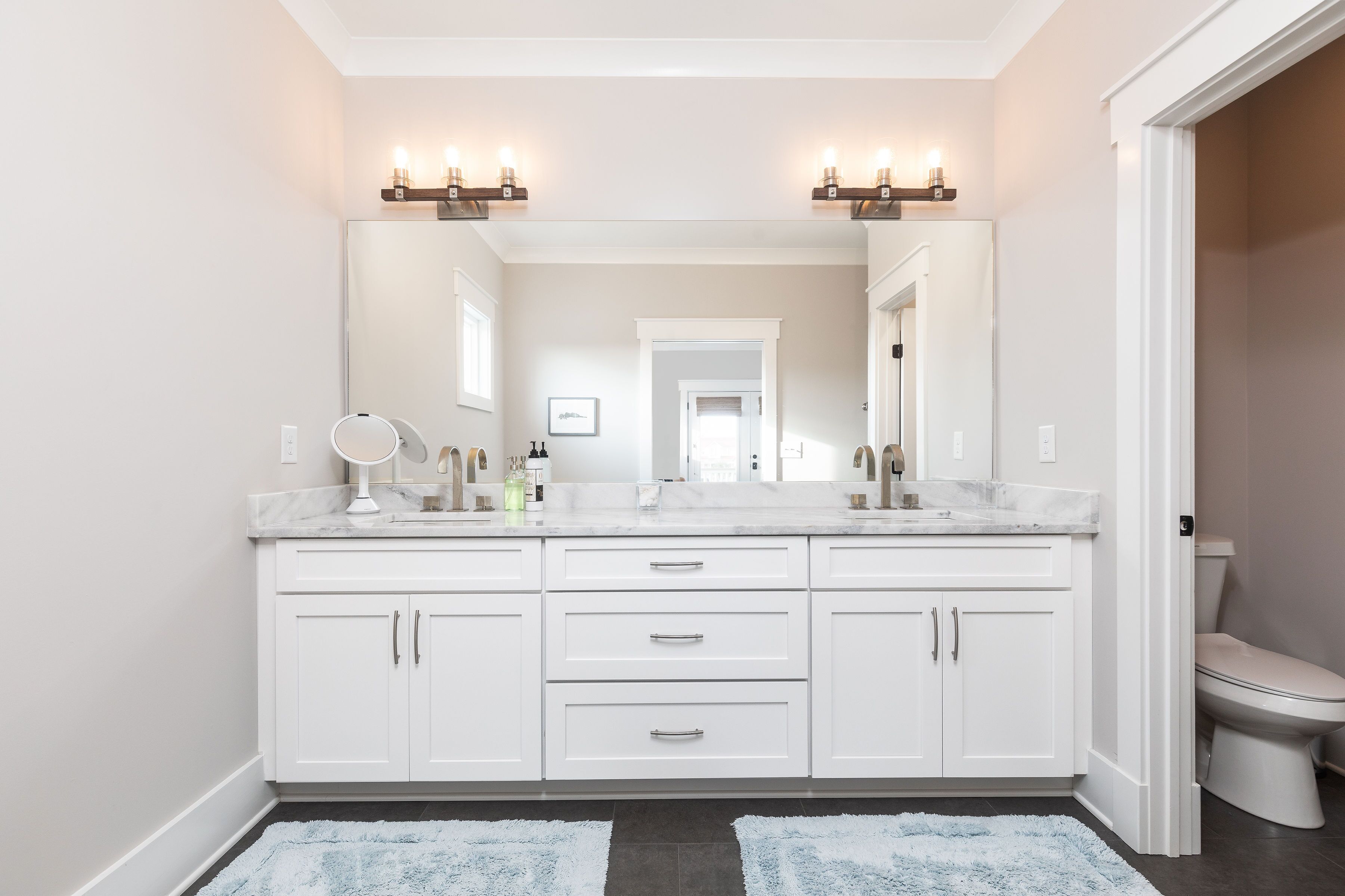 A bathroom with a double vanity, a large mirror, and a toilet.