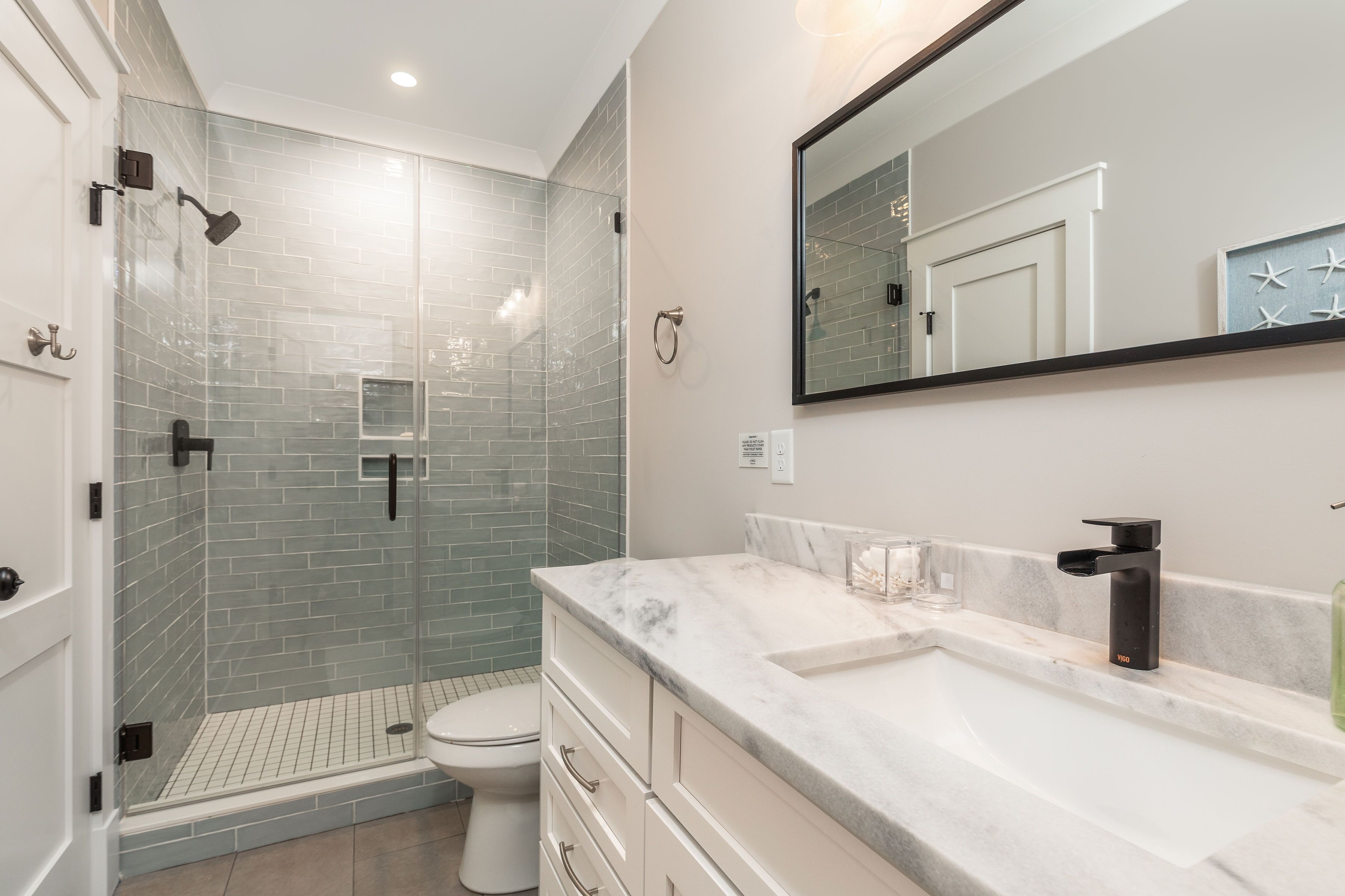 A modern bathroom with a glass-enclosed shower, a white toilet, a marble sink, and a large mirror.