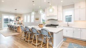 A modern kitchen with white cabinetry, a central island with bar stools, pendant lighting, and a view to the outside. - CLOSE TO CHARLESTON/ROOFTOP/LUXURY AMENTIES/POOL/OCEAN VIEW/FANTASTIC FALL RATES (Isle of Palms)