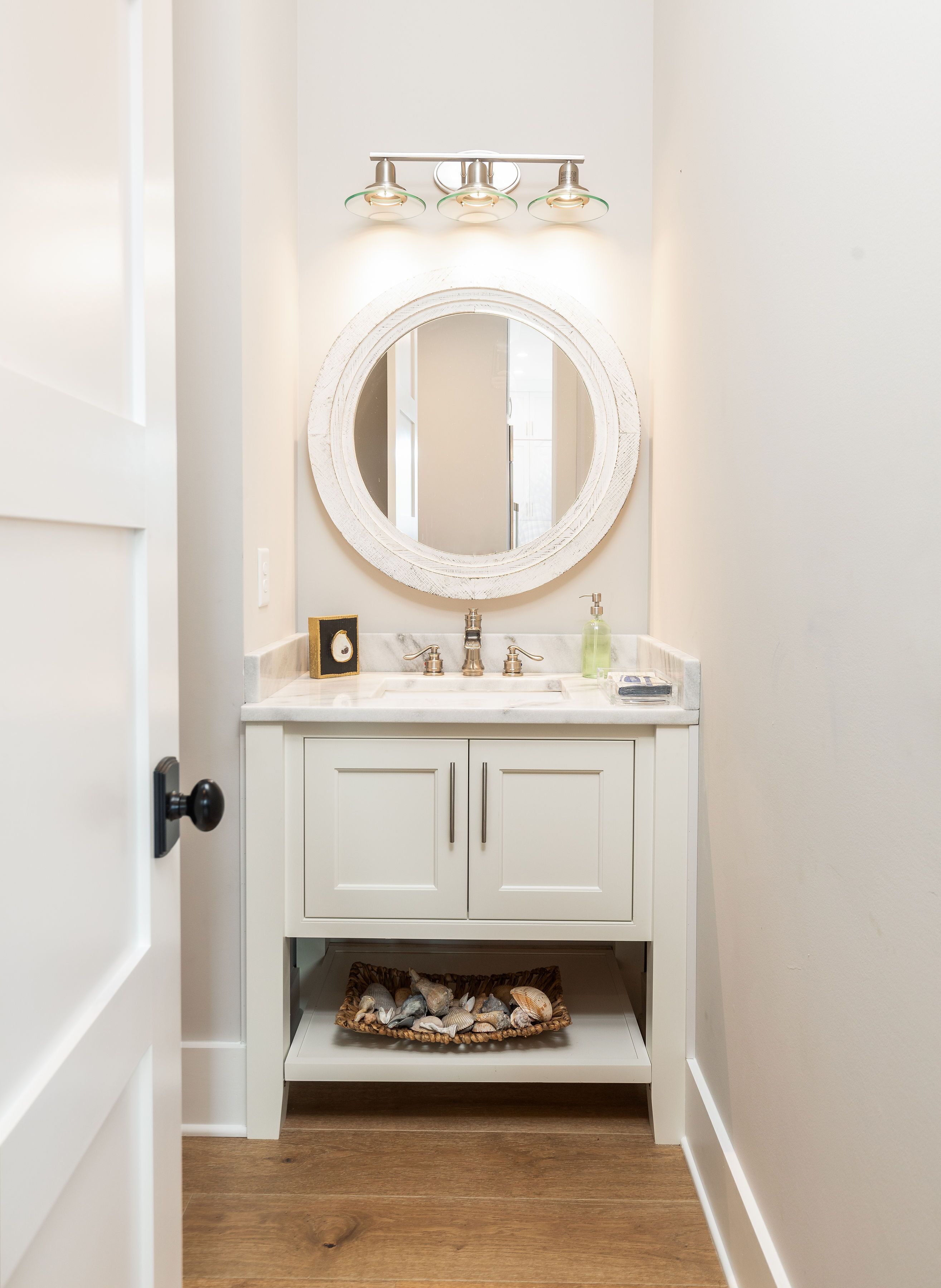 A bathroom with a white vanity, a round mirror, and a shelf with seashells.